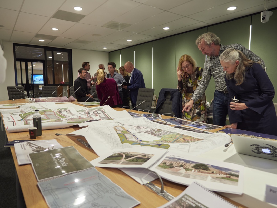 Foto van raadsleden en ambtenaren die plattegronden en illustratie bekijken